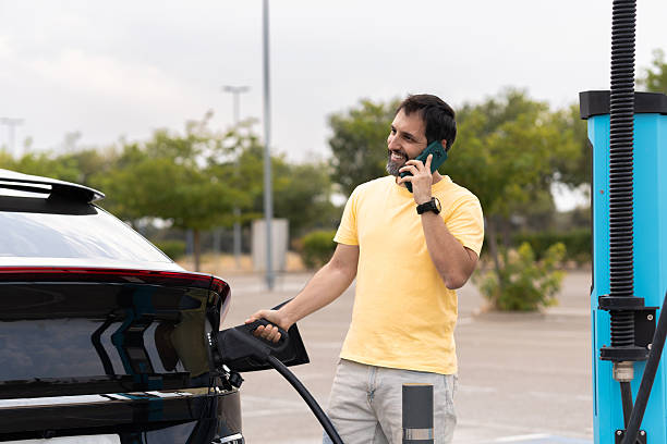 istock Smiling man charging electric car and talking on phone 2234836159