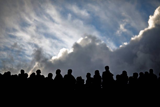 People gather in stillness beneath a cloudy sky, their forms outlined by changing light during a tranquil moment of connection.