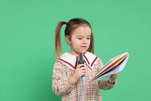 Cute girl with microphone and notebook on green background