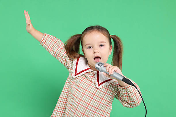 istock Cute girl with microphone singing on green background 2234839592