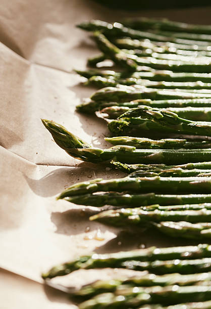 istock Green asparagus spears lie side by side on parchment paper, showcasing their freshness before being cooked for a healthy meal. 2234839898
