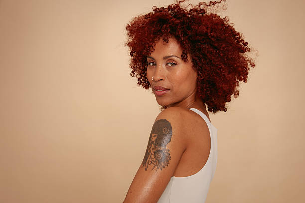An unedited studio portrait against a beige background, showcasing real skin with visible tattoos, scars, and pimples. A powerful and honest image celebrating authenticity, individuality, and the beauty of being unapologetically human.