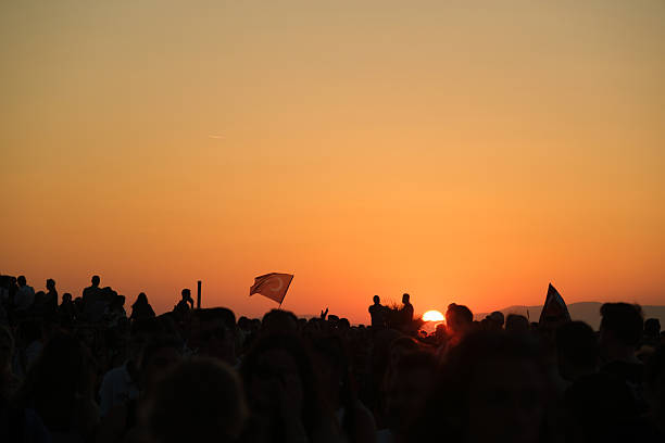 Izmir, Turkey - Sep 9 2025: Photo of waving Turkish flags in the sky with a silhouette crowd at sunset, captured on Izmir's liberation anniversary