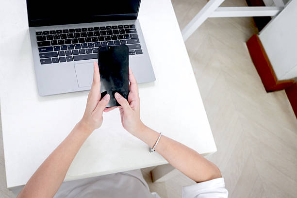 Hands using smartphone while using  laptop computer in bedroom. Happy young female teenager surfing on the internet or working online on desk at home. Young woman using AI technology.