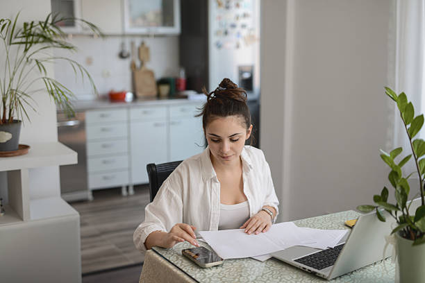istock Woman Concentrating On Budget Sheets While Using Phone For Quick Calculations At Home 2234844390