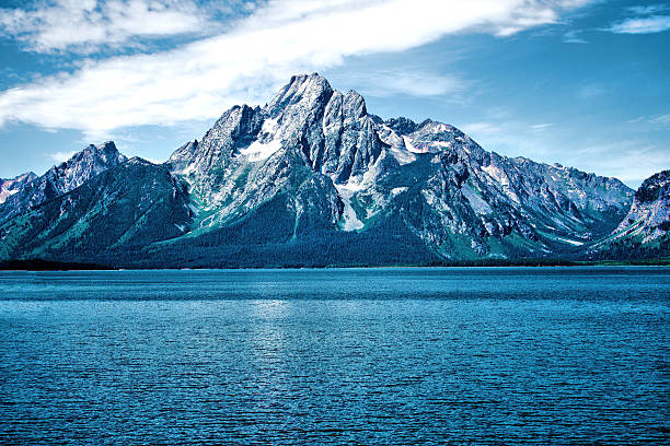 Beautiful rugged Mount Moran viewed from the calm waters of Jackson Lake on a bright day with vibrant blue skies and water.