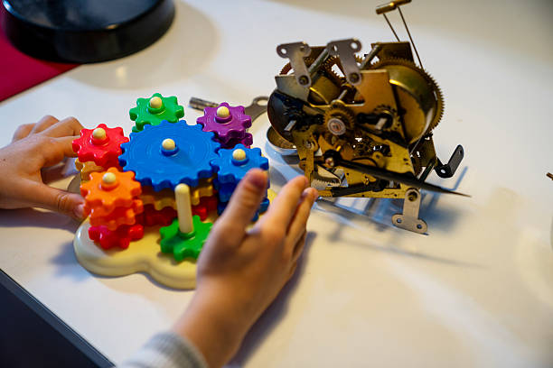 Close up photo of 6 years old boy using multicolored plastic gears for using mechanism of clockwork. Shot indoor with a full frame mirrorless camera.