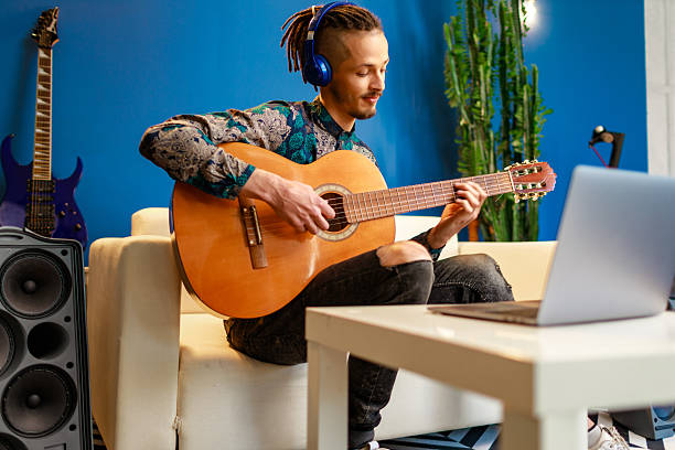 istock Young stylish caucasian man taking guitar class online at home using his laptop 2234846854