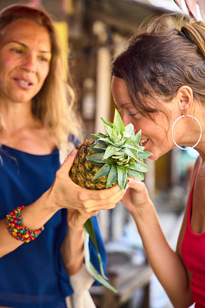 Two women appreciating a fresh pineapple in a market setting