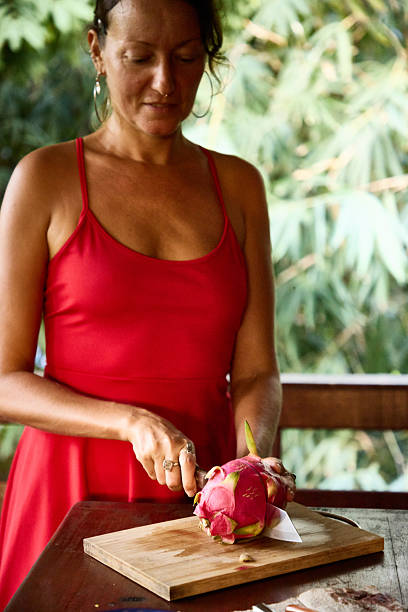 Woman Slicing Dragon Fruit in a Red Dress at an Outdoor Setting