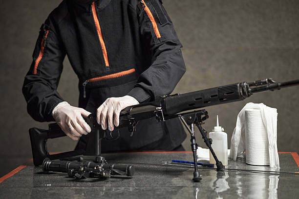 istock Middle Aged Man Cleaning Rifle with Gloves in Indoor Setting 2234852445