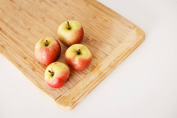 Four ripe red and yellow apples sit on a bamboo cutting board, ready for slicing, dicing, or enjoying whole, adding a touch of freshness to any culinary endeavor
