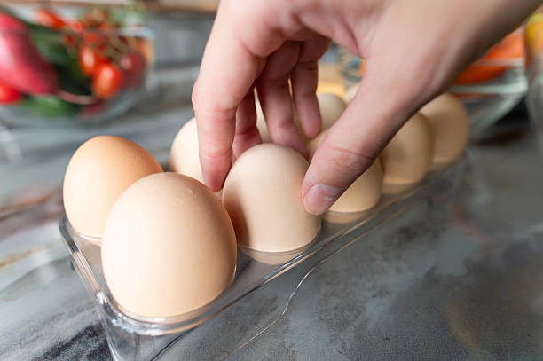 istock Human hand with eggs takes or puts one clean egg on the background of kitchen table with prepared ingredients. Food preparation concept 2234864172