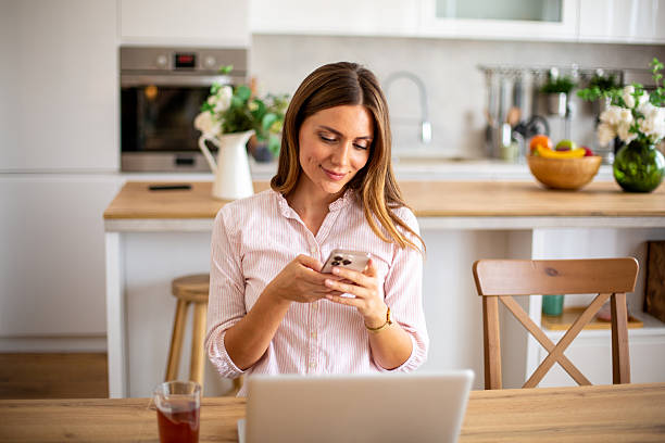 istock Young woman using smartphone and laptop in kitchen 2234866241