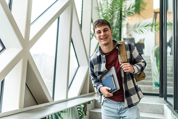 istock Smiling student carrying laptop and notebook walking in university hallway 2234869941