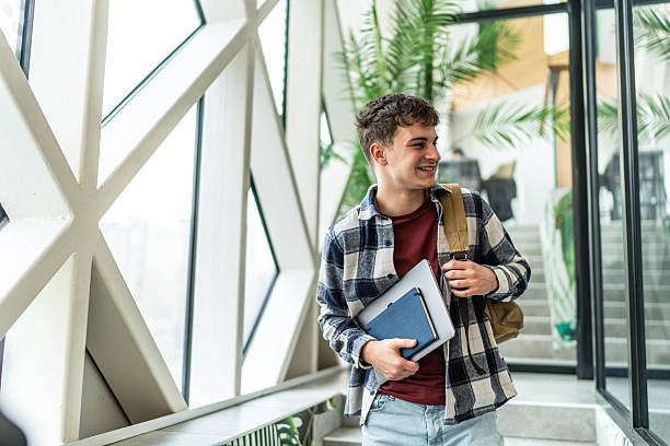 istock Smiling student walking through university hallway holding laptop and notebook 2234869943