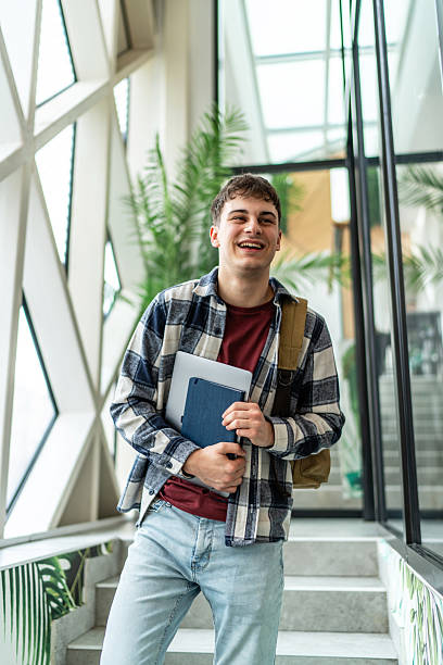 istock Smiling student walking up stairs at university holding laptop and book 2234869984