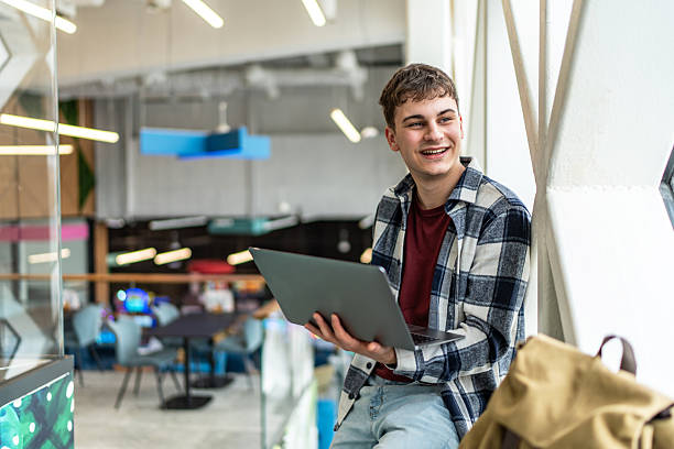 istock Young man using laptop in modern co-working space, smiling and looking away 2234870069