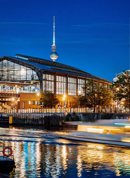 Nighttime photograph capturing a lit-up waterside building beside the Berlin Tower, reflected beautifully in the river's surface.