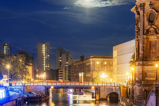 Night view in Berlin featuring illuminated buildings, a canal bridge, and atmospheric lighting emphasizing the historical and urban cityscape.