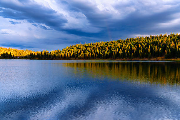 Dramatic light illuminating the mountainside with steel-blue storm cloud and faint rainbow in sky.