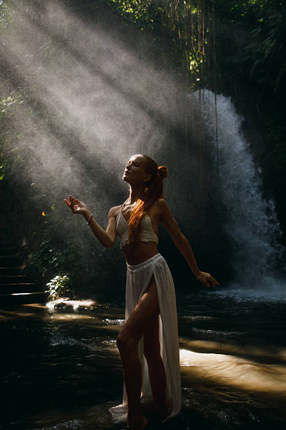 istock Woman Dancing Gracefully Beneath Sunlit Tropical Waterfall in Lush Forest 2234884790
