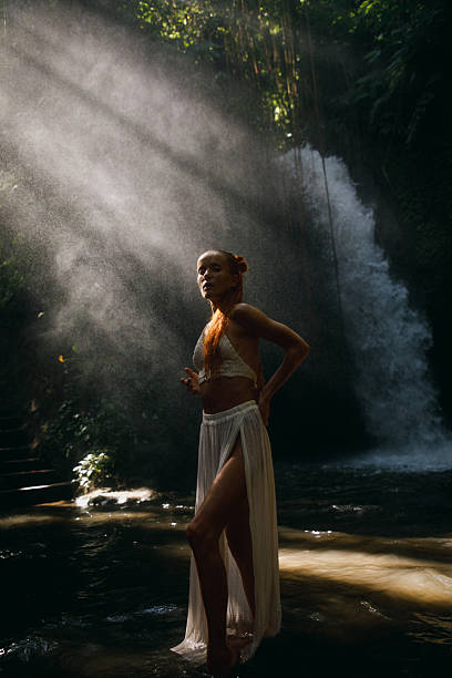 Woman standing by a cascading waterfall illuminated by soft sunlight