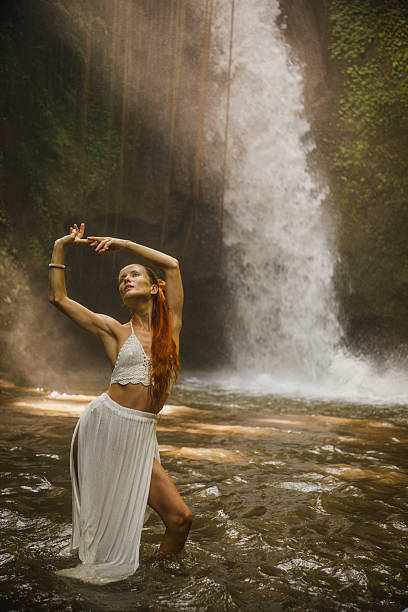 istock Graceful dancer poses in flowing white dress beneath lush waterfall 2234884993