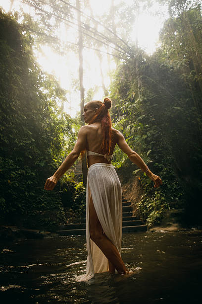 istock Woman walking through a serene jungle stream with sunlight filtering through trees 2234884997