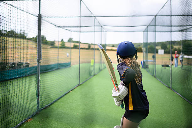 istock Back view through net as young female batsman stands ready to hit the ball 2234886734