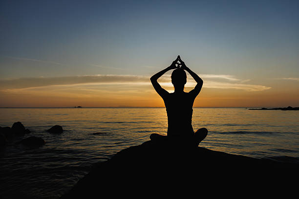 Silhouette practicing meditation by the sea during a peaceful sunset