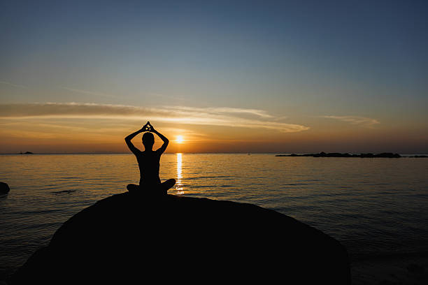 Silhouette practicing yoga at sunset on a beach with serene ocean view