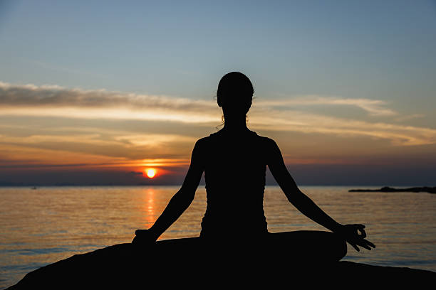 istock Silhouette of meditator at sunset near calm ocean setting 2234888571