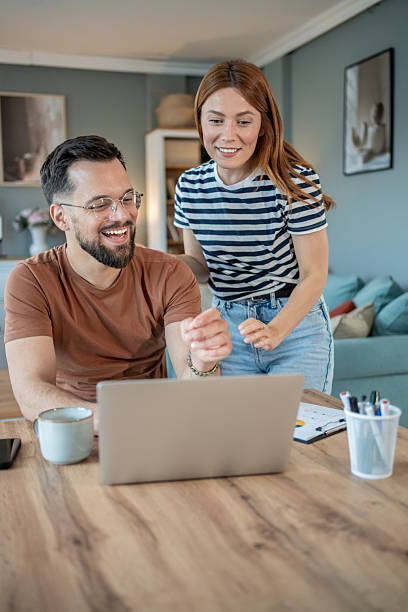 istock Young couple smiling and working on laptop at home 2234889331