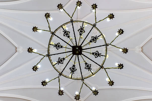 Symmetrical circular chandelier captured from directly below, forming a starburst pattern against pale Gothic vaults. Graphic architectural composition perfect for design, pattern, and heritage uses.