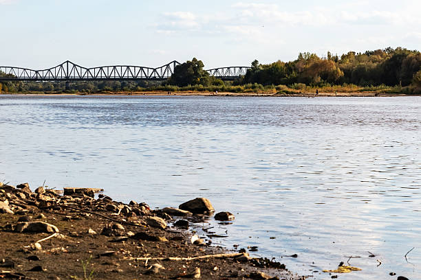 istock Riverbank with rocks and distant truss bridge under blue sky 2234890221