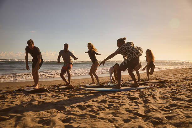istock Group of friends practicing surfing techniques on the beach at sunset 2234890285