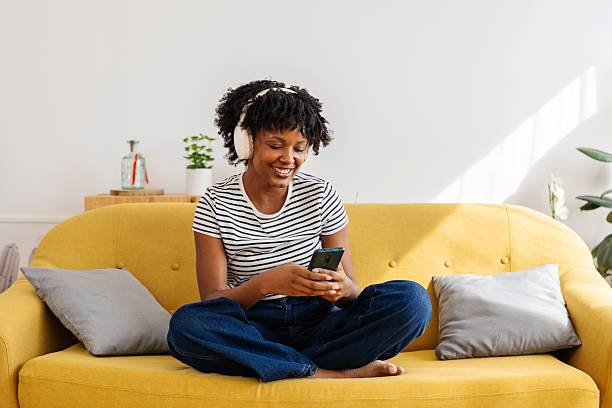 istock Happy young black woman using mobile phone relaxing on sofa at home 2234891755