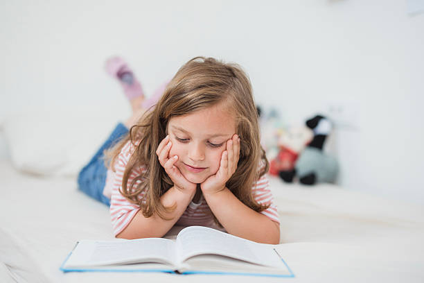 istock Cute little girl reading a book on her bed 2234892853