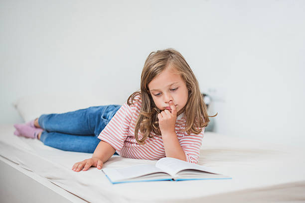 istock Elementary age girl reading a book on bed in bedroom 2234892912