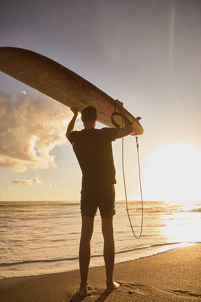 istock Man holding a surfboard on the beach at sunset ready for surfing 2234894613