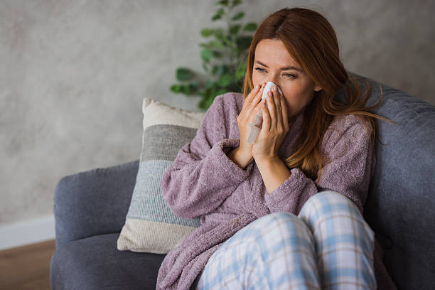 istock Sick young woman blowing her nose while sitting on sofa at home 2234895141