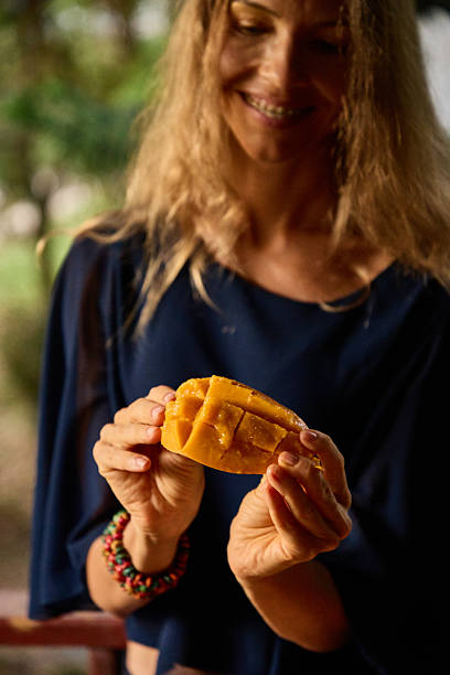 Woman holding a fresh mango slice with a cheerful and natural setting