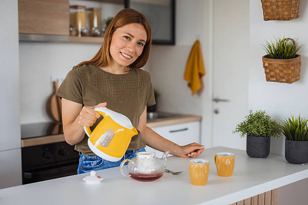 Woman pouring hot water into teapot in modern kitchen