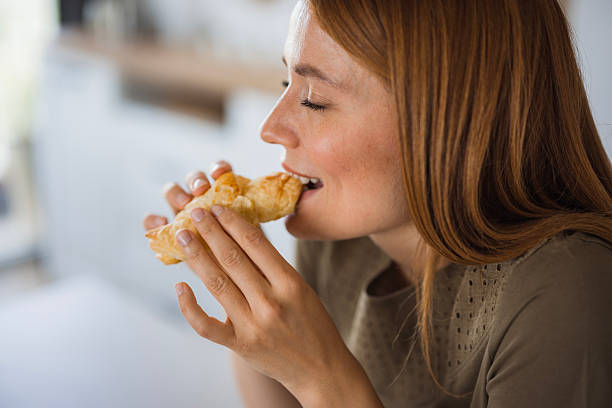 istock Young woman enjoying eating croissant in kitchen 2234899238