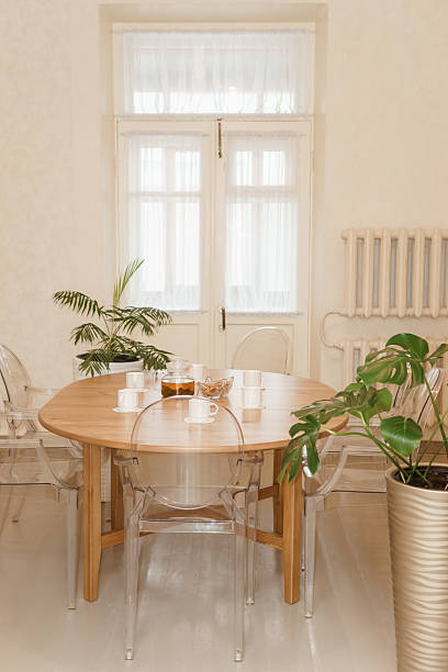 istock Cozy dining setting featuring a round wooden table surrounded by transparent chairs, complemented by lush green potted plants, creating a warm and inviting interior atmosphere. 2234900236