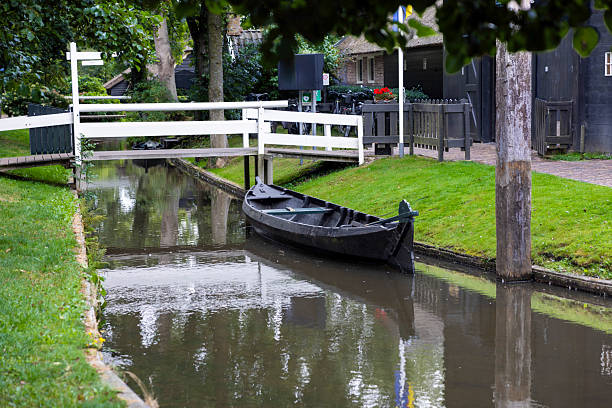 Scenic view of a traditional Dutch thatched-roof house surrounded by a vibrant flower garden along a peaceful canal in Giethoorn, Netherlands. A picturesque and idyllic summer travel destination.