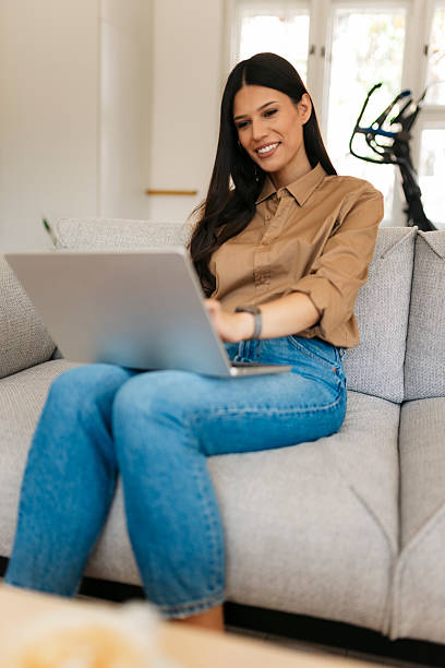 istock Young woman working remotely from home using laptop on sofa 2234908930