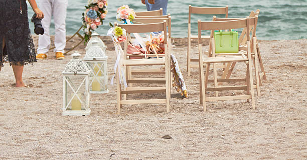 istock Back view of preparations for wedding ceremony on beach: chairs for spectators, wedding photographer, photo zone ,decorated with flowers and decorative lanterns. Concept: wedding, celebration, sea. 2234909669