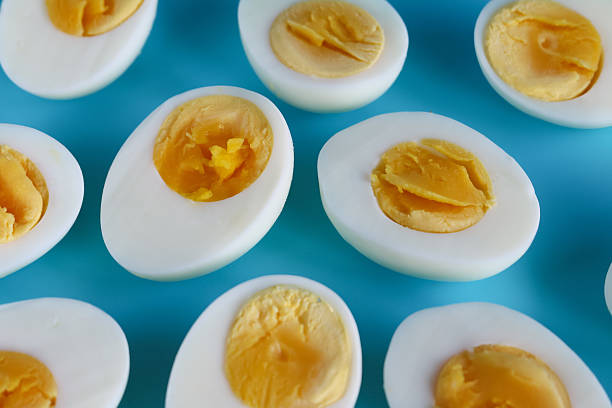 Stock photo showing close-up, elevated view of hard-boiled chicken egg halves isolated on a blue background.